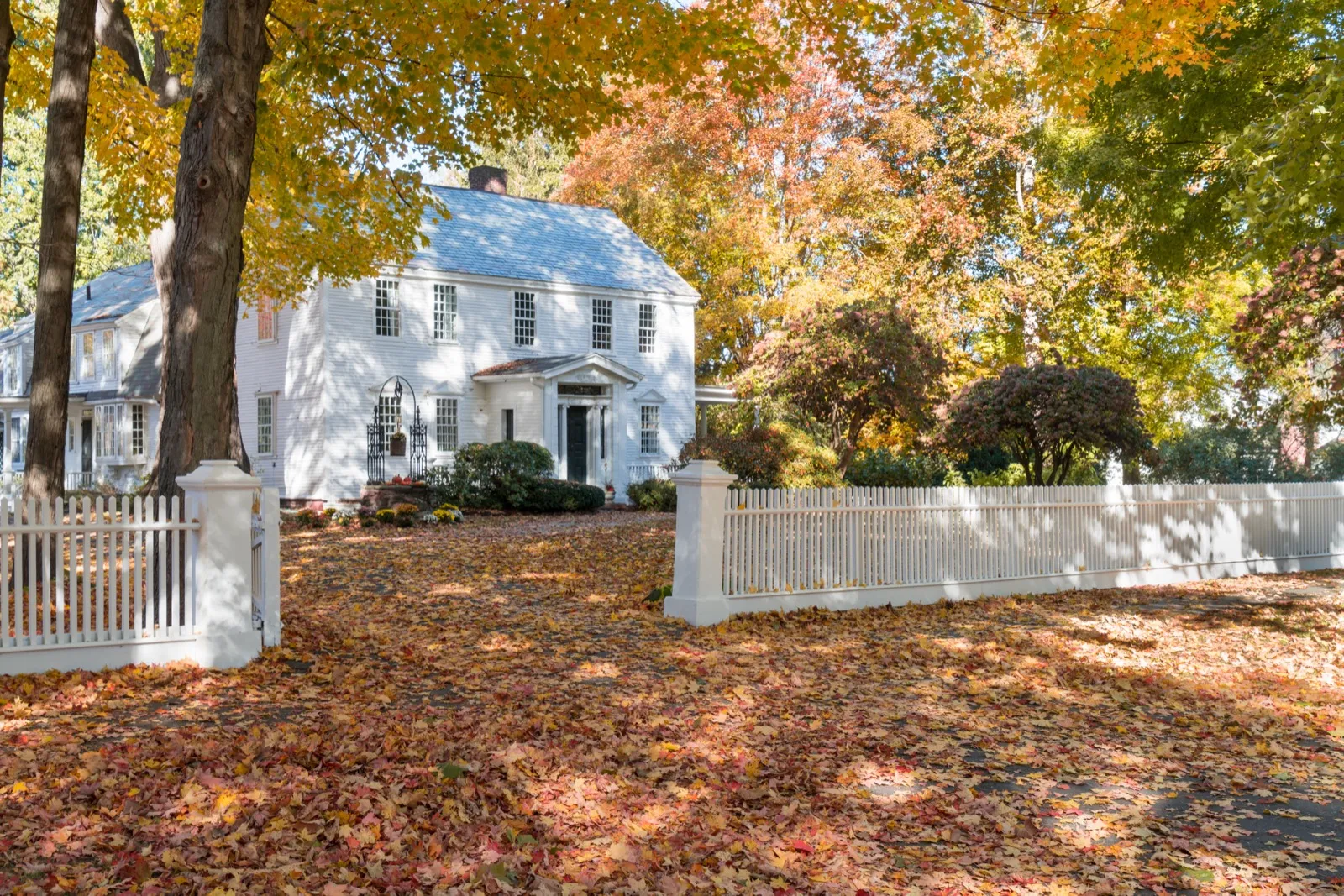 Historic white colonial home with a picket fence and autumn foliage in Wrentham, MA